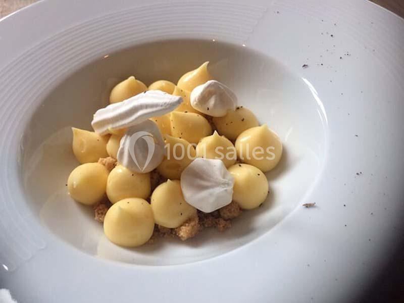 Dessert composé de petites pointes de crème jaune, morceaux de meringue blanche et éclats de biscuit dans une assiette…