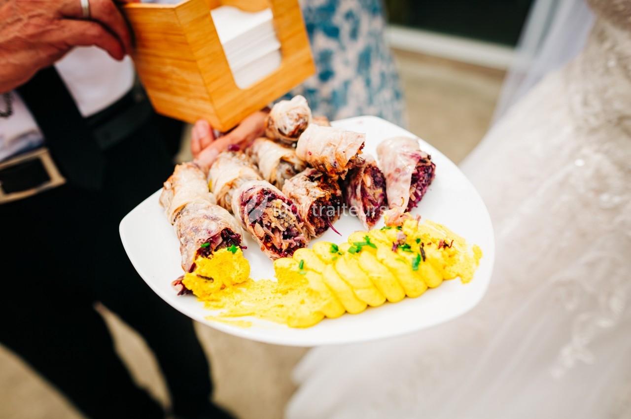 Assiette contenant des rouleaux garnis et une purée jaune décorée, tenue par une personne lors d'un événement.