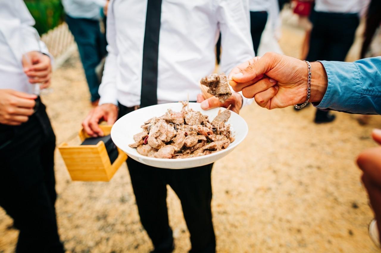 Un serveur propose un plat de morceaux de viande à des invités lors d'un événement en extérieur.