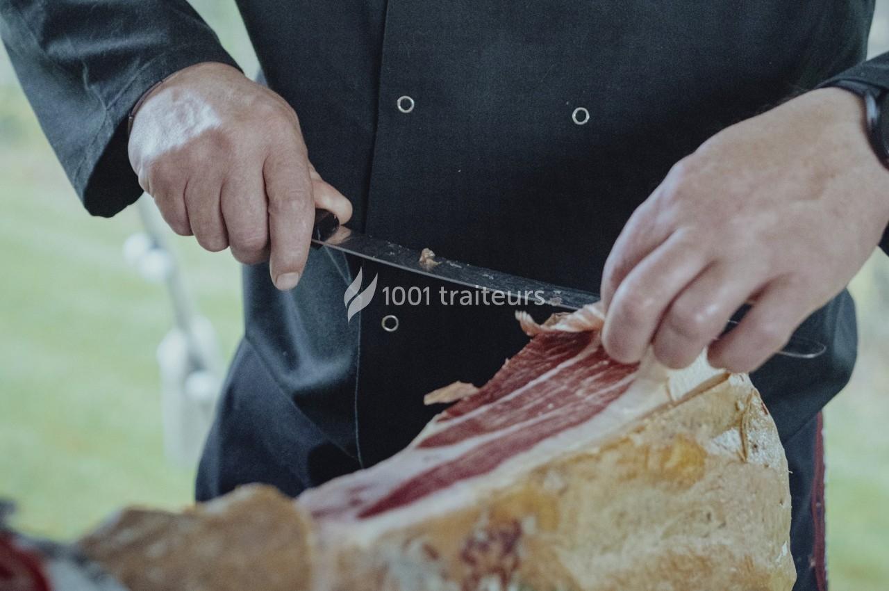 Un cuisinier découpe finement une tranche de jambon cru à l'aide d'un couteau.