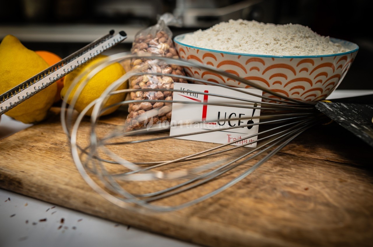 Bol de farine, fouet métallique, citrons, zesteur, beurre et noisettes posés sur une planche en bois.