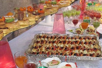 Un homme en tenue traditionnelle sert du thé près d'une table garnie de pâtisseries et de verres dans une salle lumineuse.