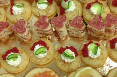 Un homme en tenue traditionnelle sert du thé près d'une table garnie de pâtisseries et de verres dans une salle lumineuse.