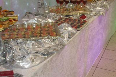 Un homme en tenue traditionnelle sert du thé près d'une table garnie de pâtisseries et de verres dans une salle lumineuse.