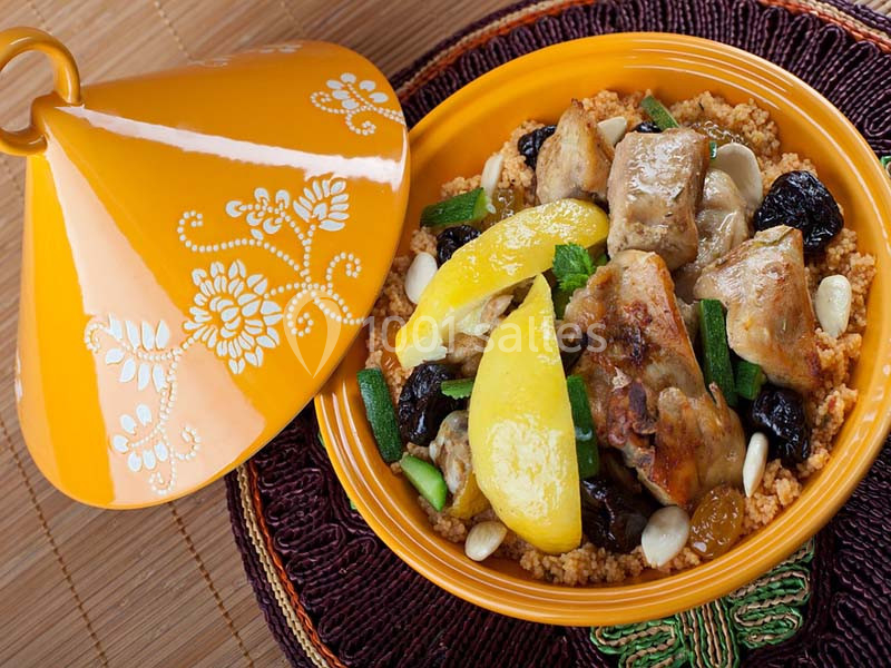 Tajine de poulet avec légumes, pruneaux, amandes et semoule, présenté dans un plat traditionnel décoré.