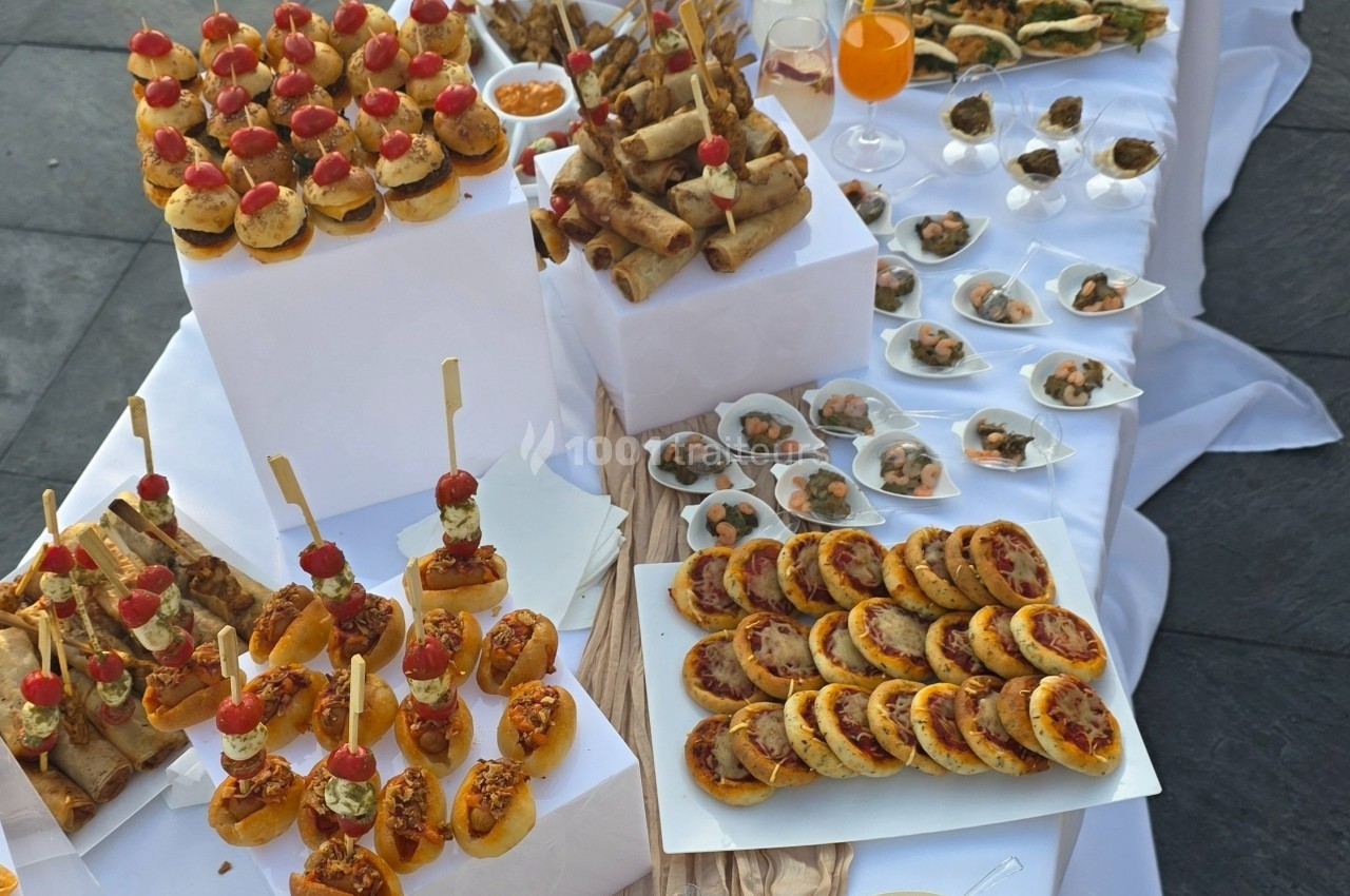 Buffet de bouchées apéritives variées disposées sur des présentoirs, incluant mini-pizzas, brochettes et rouleaux.