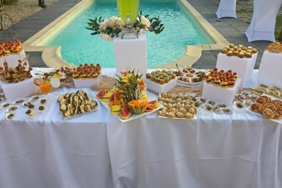 Un homme en tenue traditionnelle sert du thé près d'une table garnie de pâtisseries et de verres dans une salle lumineuse.