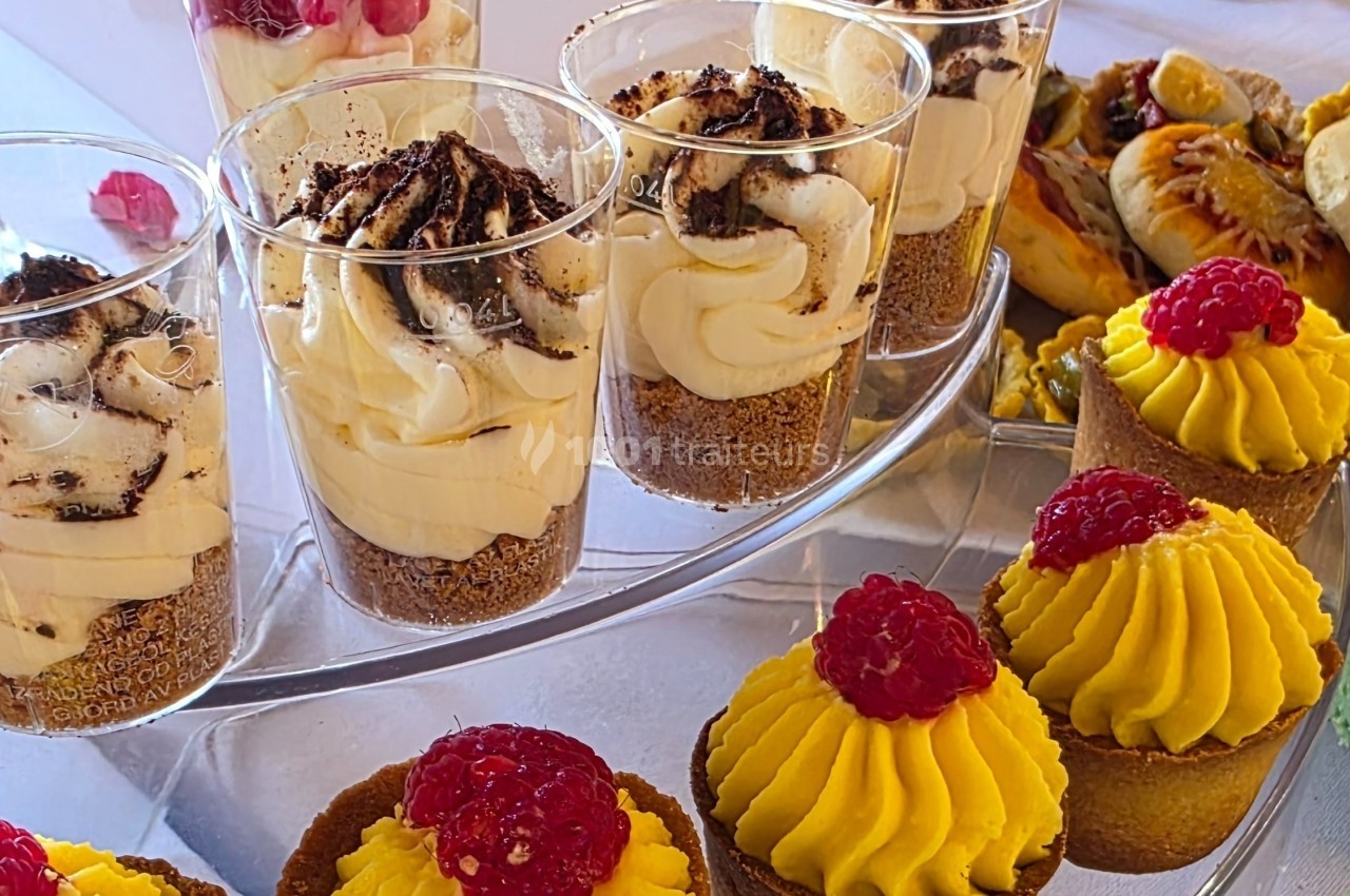 Desserts variés sur un plateau, incluant verrines à la crème et gâteaux garnis de framboises.