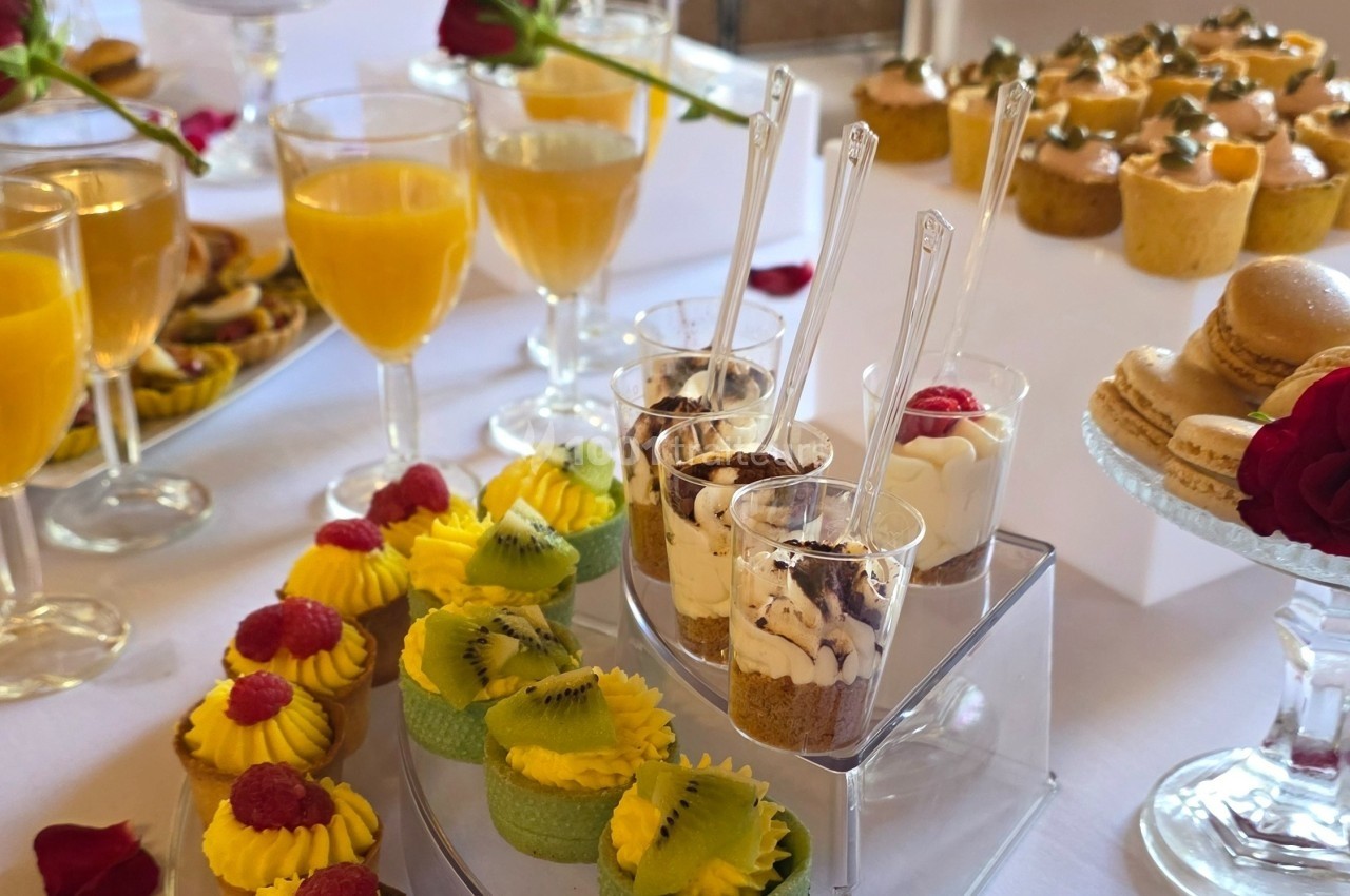 Desserts variés sur une table, incluant verrines, macarons, pâtisseries aux fruits et verres de jus d'orange.