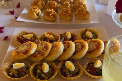 Un homme en tenue traditionnelle sert du thé près d'une table garnie de pâtisseries et de verres dans une salle lumineuse.