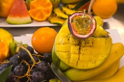 Un homme en tenue traditionnelle sert du thé près d'une table garnie de pâtisseries et de verres dans une salle lumineuse.