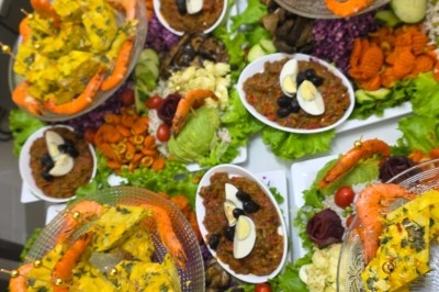 Un homme en tenue traditionnelle sert du thé près d'une table garnie de pâtisseries et de verres dans une salle lumineuse.