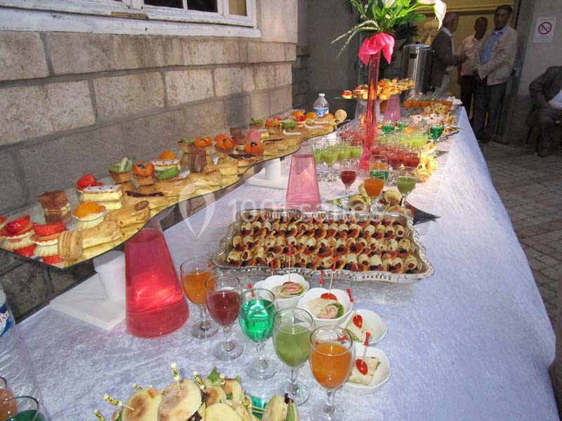 Buffet avec amuse-bouches variés, verrines colorées et pâtisseries disposés sur une table blanche décorée.
