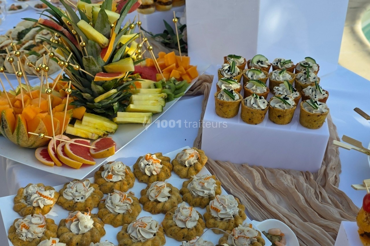 Plateau de buffet avec fruits frais, verrines garnies et bouchées salées disposés sur une table blanche.