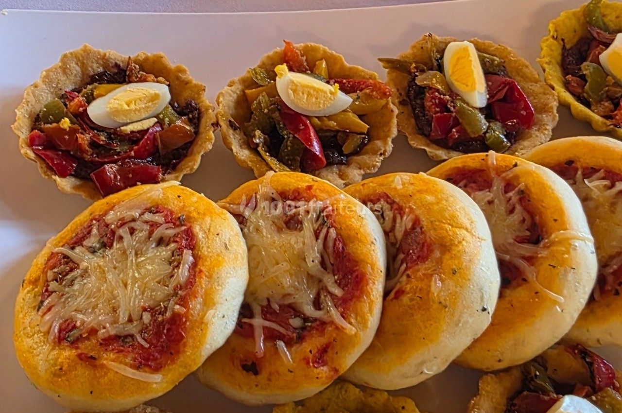 Assortiment de mini pizzas au fromage et de tartelettes garnies de légumes et quartiers d'œufs durs.