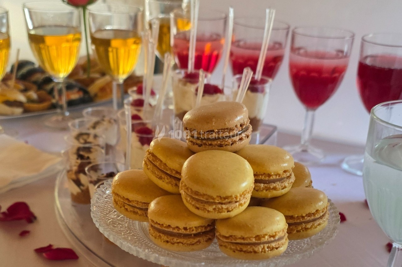 Plateau de macarons jaunes sur une table avec des verrines et des boissons colorées en arrière-plan.