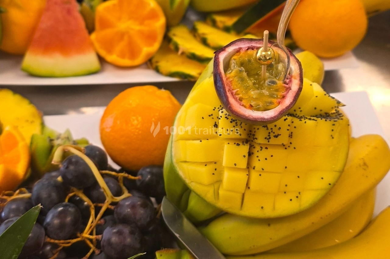 Assortiment de fruits frais comprenant mangue découpée, fruit de la passion, raisins, oranges et pastèque.