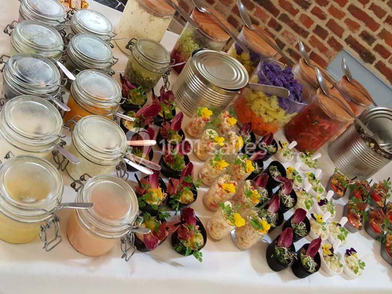 Buffet coloré avec verrines, bocaux de sauces et légumes variés disposés sur une table blanche.