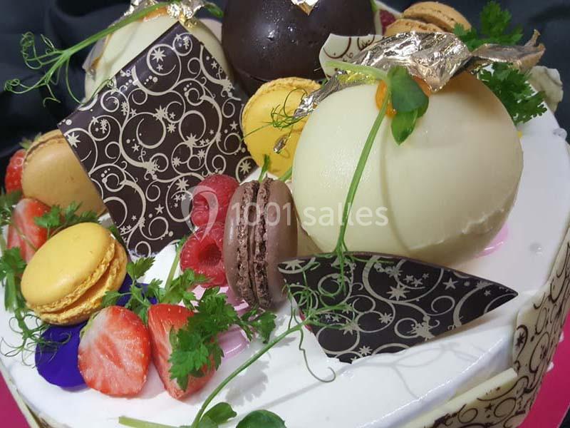 Dessert décoré avec des macarons, fraises, feuilles en chocolat, fleurs comestibles et touches de feuilles d'or.