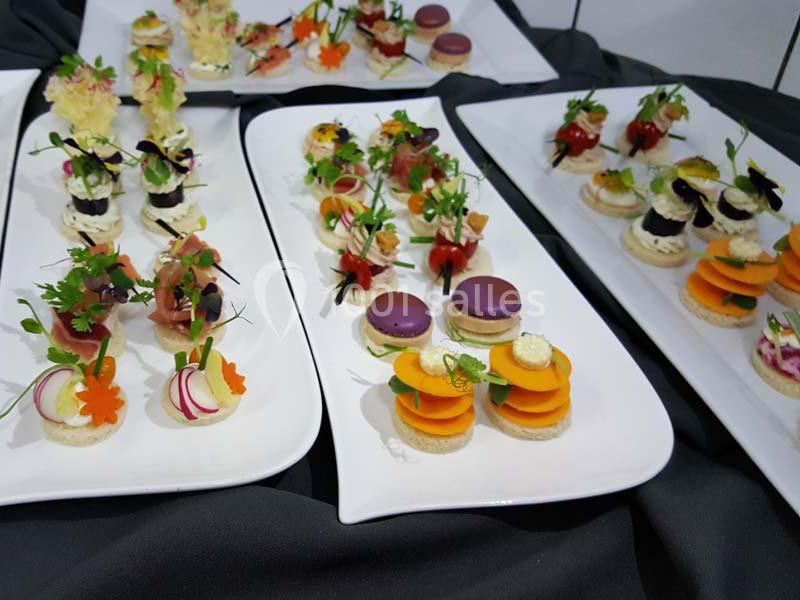 Assortiment de canapés et amuse-bouches colorés disposés sur des plateaux blancs sur une nappe sombre.