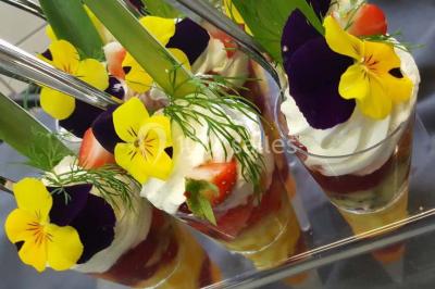 Dessert décoré avec des macarons, fraises, feuilles en chocolat, fleurs comestibles et touches de feuilles d'or.