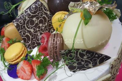 Dessert décoré avec des macarons, fraises, feuilles en chocolat, fleurs comestibles et touches de feuilles d'or.