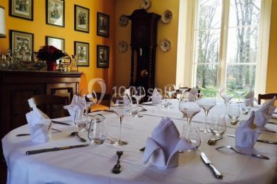 Table et chaises en bois disposées sur du gravier, face à un jardin verdoyant avec buissons et pelouse.