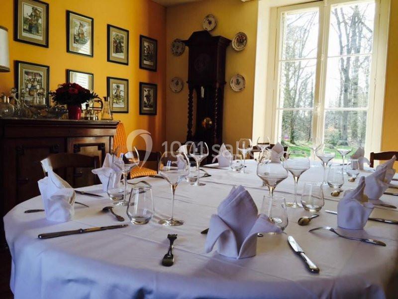 Table ronde élégamment dressée avec serviettes pliées, verres et couverts, dans une salle lumineuse aux murs jaunes.