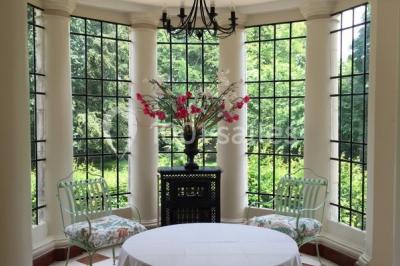 Table et chaises en bois disposées sur du gravier, face à un jardin verdoyant avec buissons et pelouse.