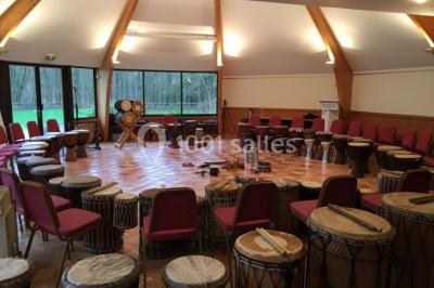 Table et chaises en bois disposées sur du gravier, face à un jardin verdoyant avec buissons et pelouse.