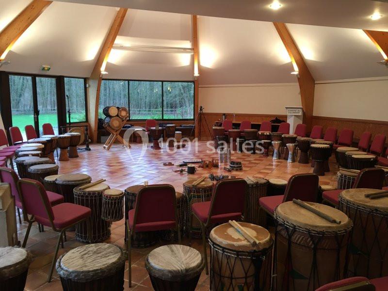 Salle circulaire avec chaises disposées autour de djembés et autres percussions, éclairée par des fenêtres et des lumières…
