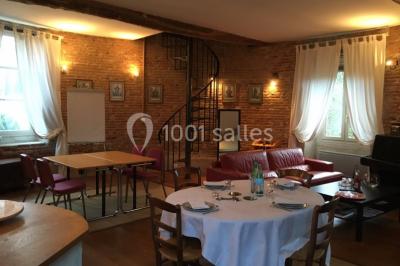 Table et chaises en bois disposées sur du gravier, face à un jardin verdoyant avec buissons et pelouse.