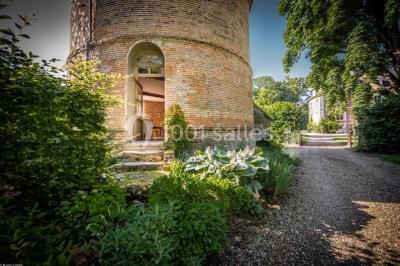Table et chaises en bois disposées sur du gravier, face à un jardin verdoyant avec buissons et pelouse.