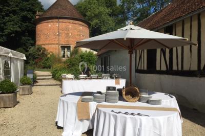 Table et chaises en bois disposées sur du gravier, face à un jardin verdoyant avec buissons et pelouse.