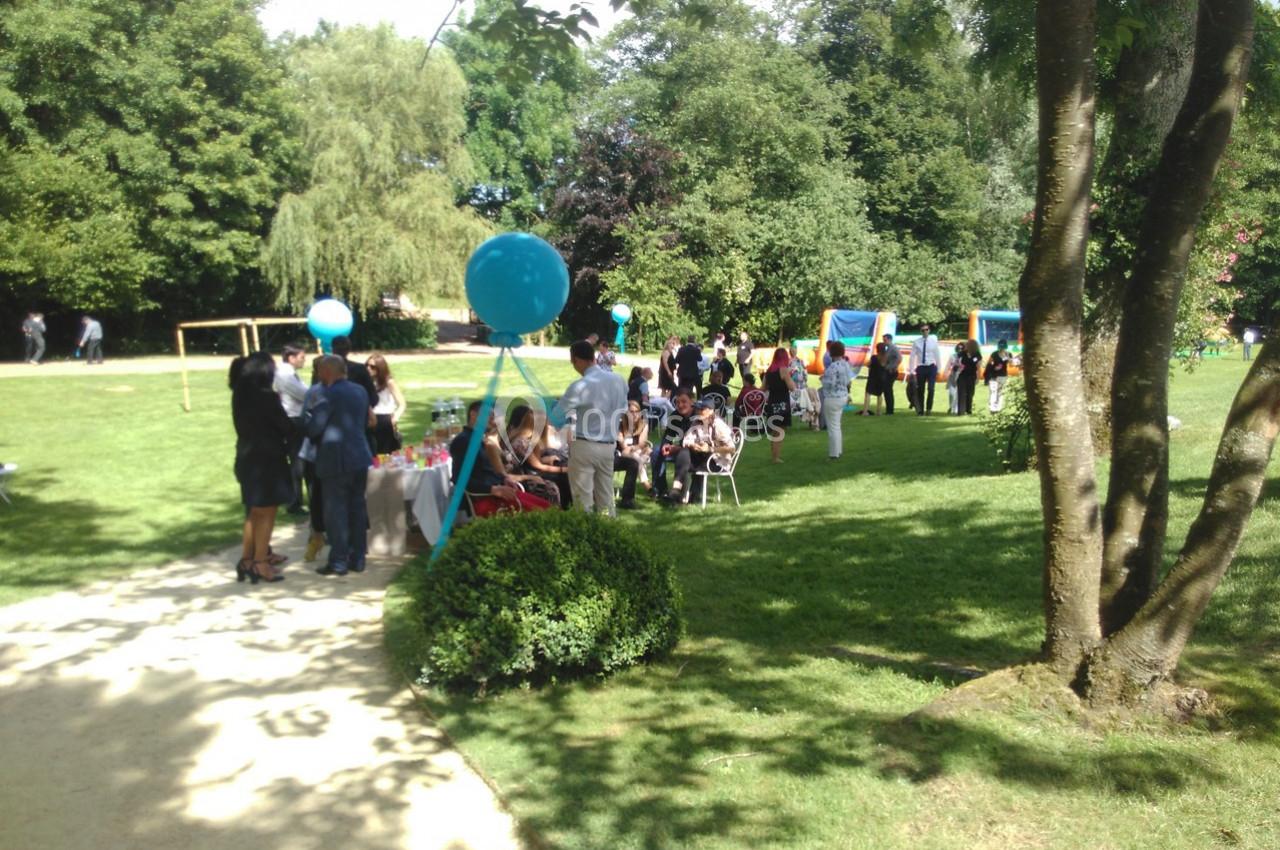 Groupe de personnes rassemblées dans un parc verdoyant autour de stands et de tables lors d'un événement en plein air.