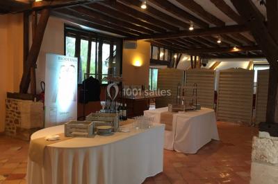 Table et chaises en bois disposées sur du gravier, face à un jardin verdoyant avec buissons et pelouse.