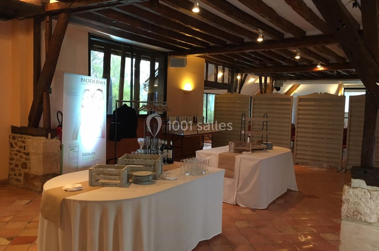 Salle avec poutres apparentes, tables dressées avec vaisselle et présentoirs, éclairage doux et panneaux en arrière-plan.