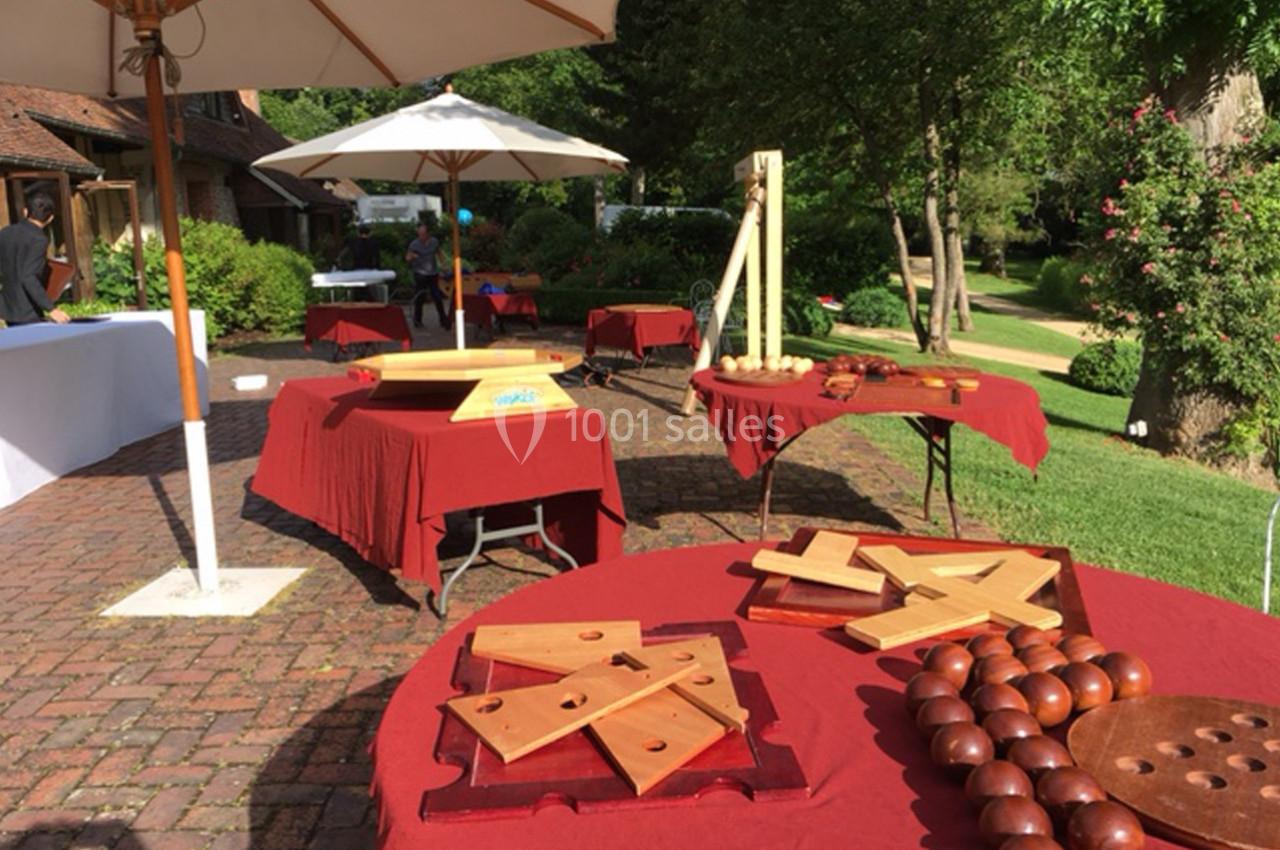 Tables avec nappes rouges disposées en extérieur, présentant des jeux en bois sous des parasols blancs.
