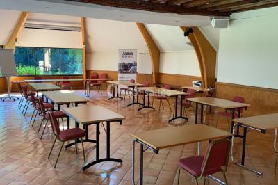 Table et chaises en bois disposées sur du gravier, face à un jardin verdoyant avec buissons et pelouse.