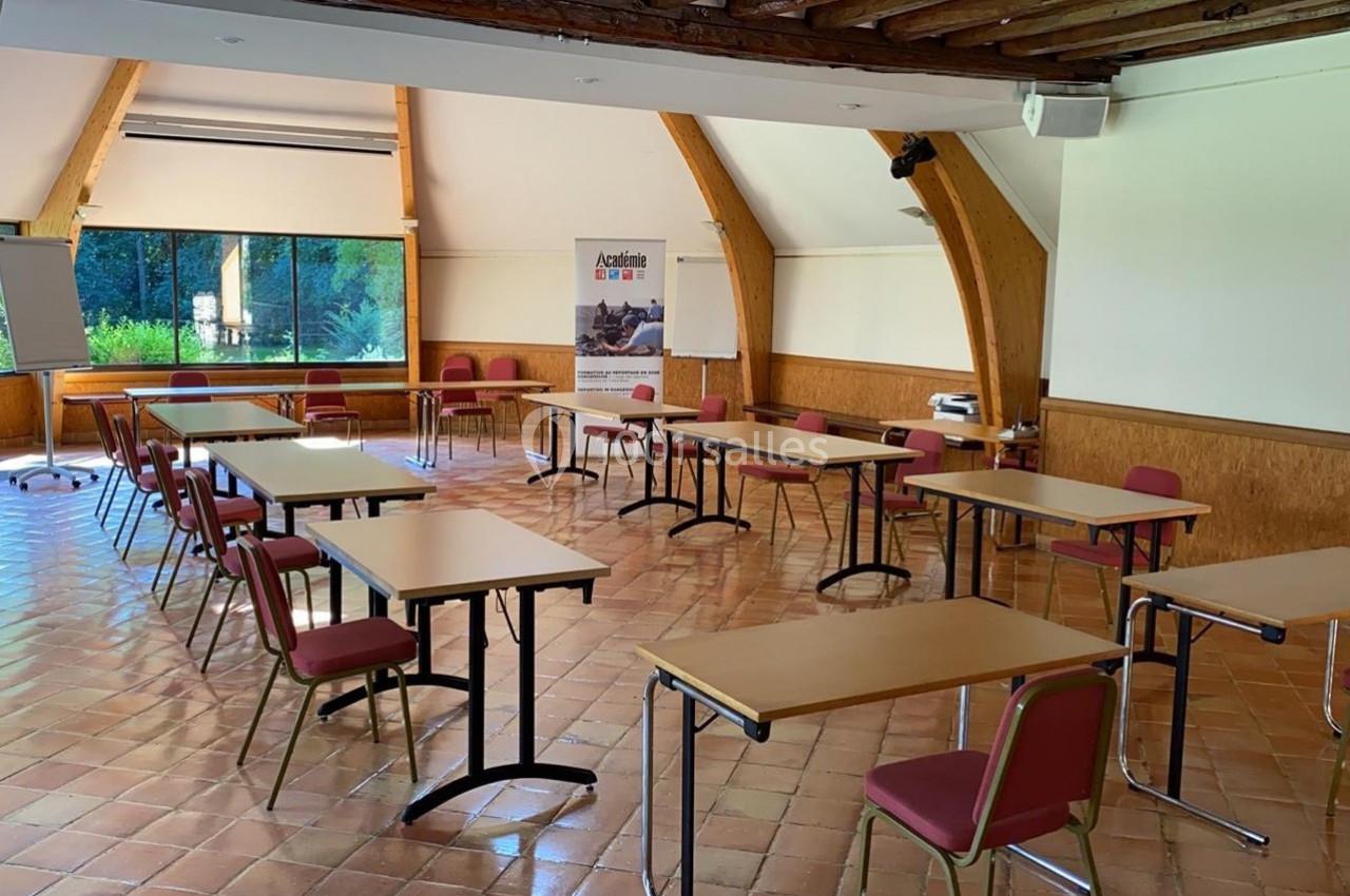 Salle de réunion lumineuse avec des tables et chaises disposées en U, un tableau blanc et un vidéoprojecteur.