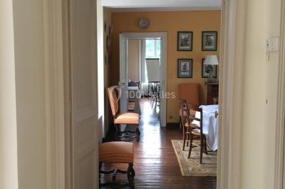Table et chaises en bois disposées sur du gravier, face à un jardin verdoyant avec buissons et pelouse.