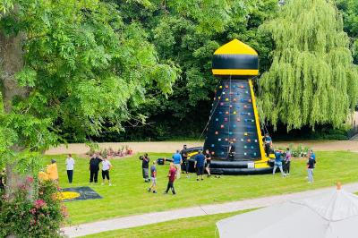 Table et chaises en bois disposées sur du gravier, face à un jardin verdoyant avec buissons et pelouse.