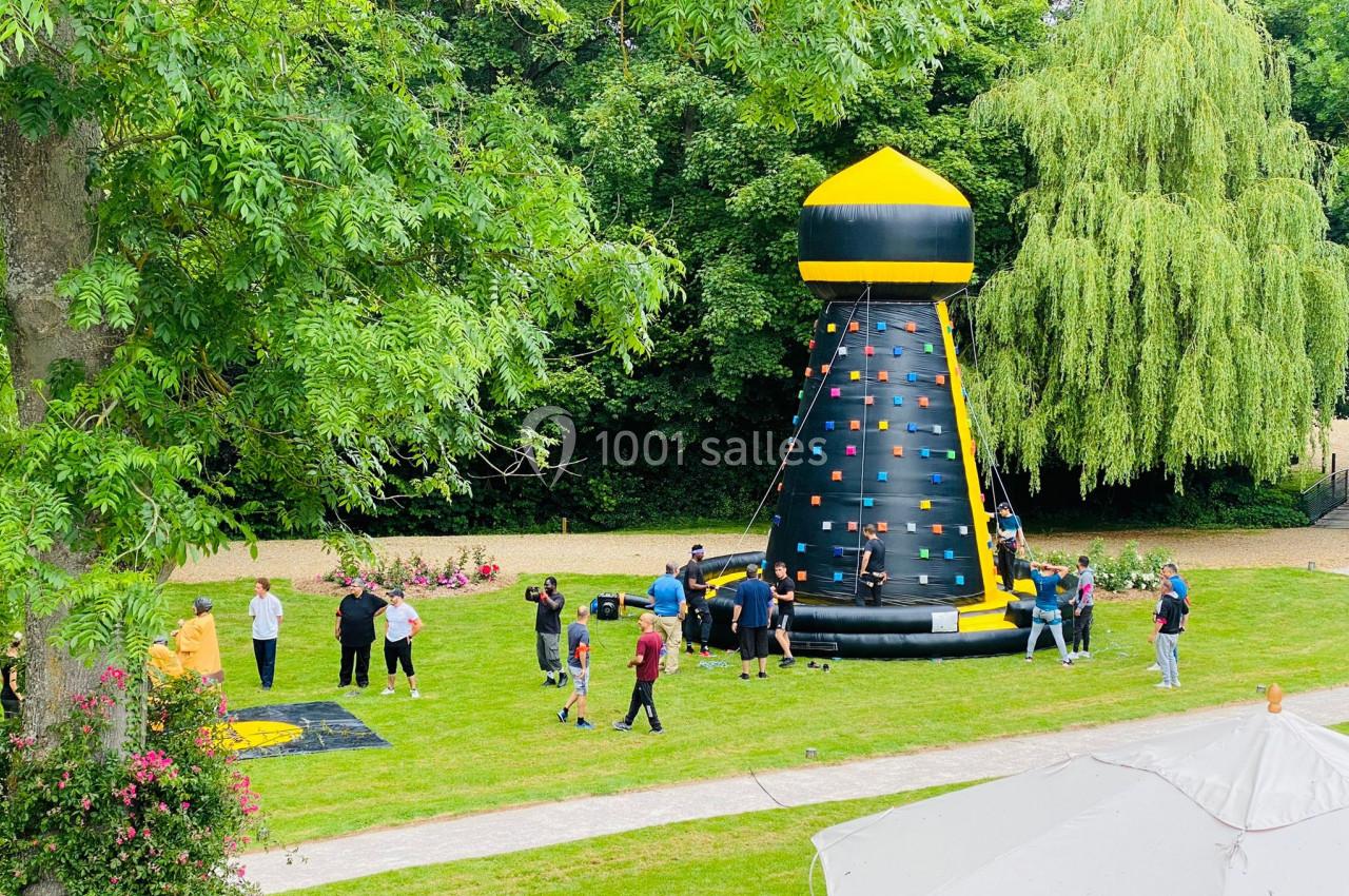 Des personnes participent à une activité autour d'une structure gonflable d'escalade dans un parc verdoyant.