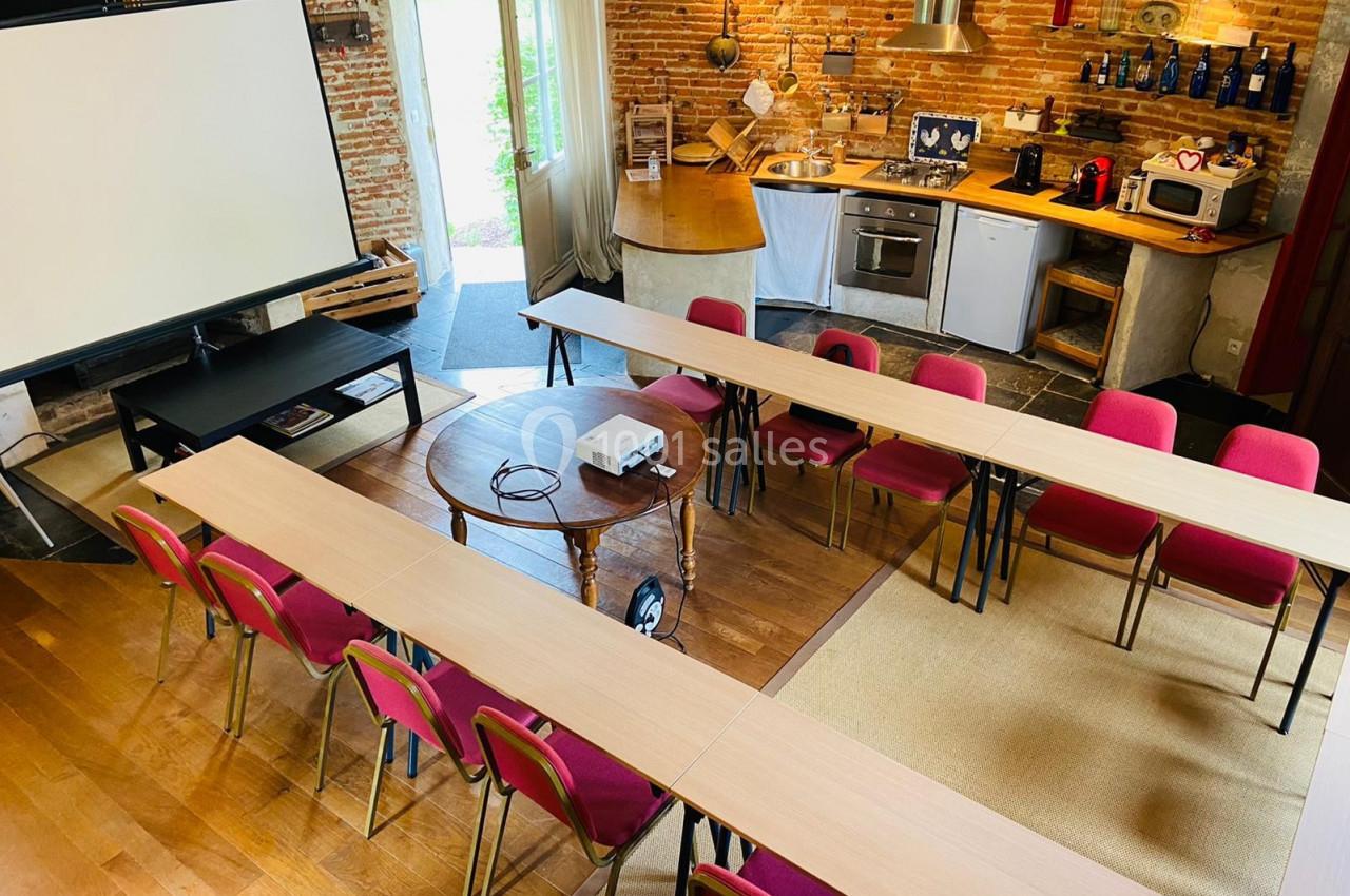 Salle aménagée pour une réunion, avec des tables en U, des chaises rouges, un projecteur et un écran de projection.