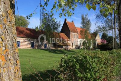 Tour en briques avec toit en ardoise, entourée de bâtiments ruraux et d'arbres, sous un ciel dégagé.