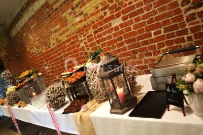 Tour en briques avec toit en ardoise, entourée de bâtiments ruraux et d'arbres, sous un ciel dégagé.