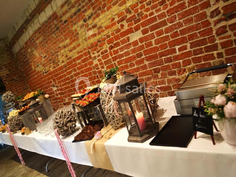 Buffet décoré avec des plats variés, lanternes et éléments rustiques, disposé devant un mur en briques rouges.