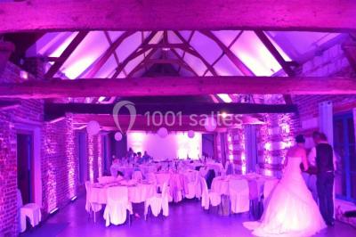 Tour en briques avec toit en ardoise, entourée de bâtiments ruraux et d'arbres, sous un ciel dégagé.