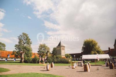 Tour en briques avec toit en ardoise, entourée de bâtiments ruraux et d'arbres, sous un ciel dégagé.