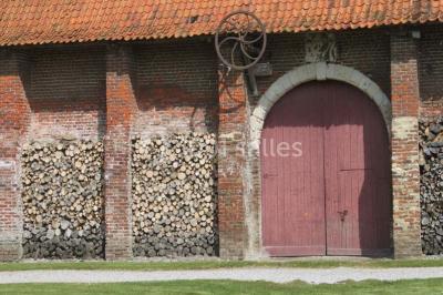 Tour en briques avec toit en ardoise, entourée de bâtiments ruraux et d'arbres, sous un ciel dégagé.